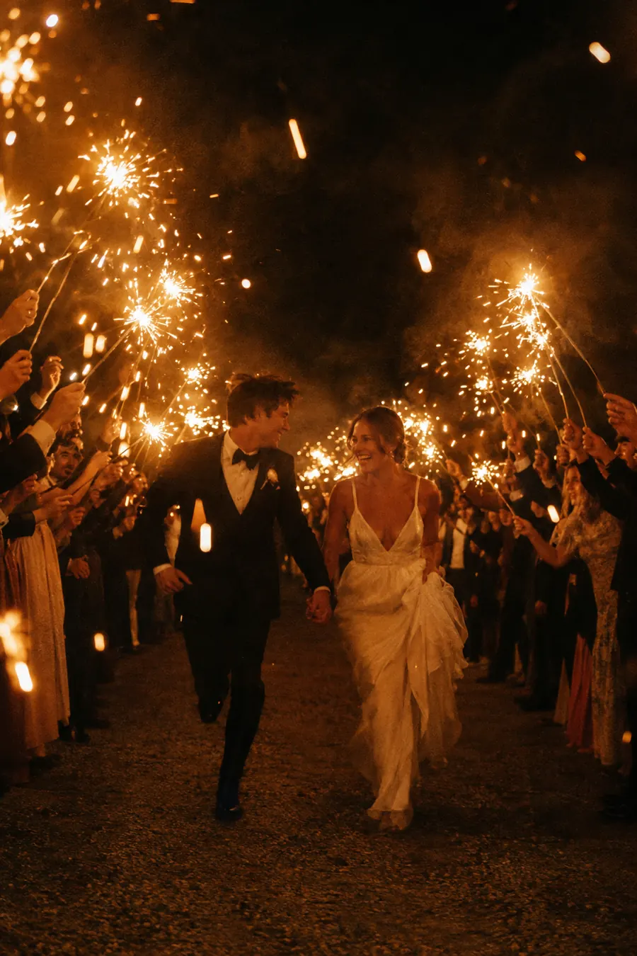A couple running through a tunnel of glowing sparklers at night